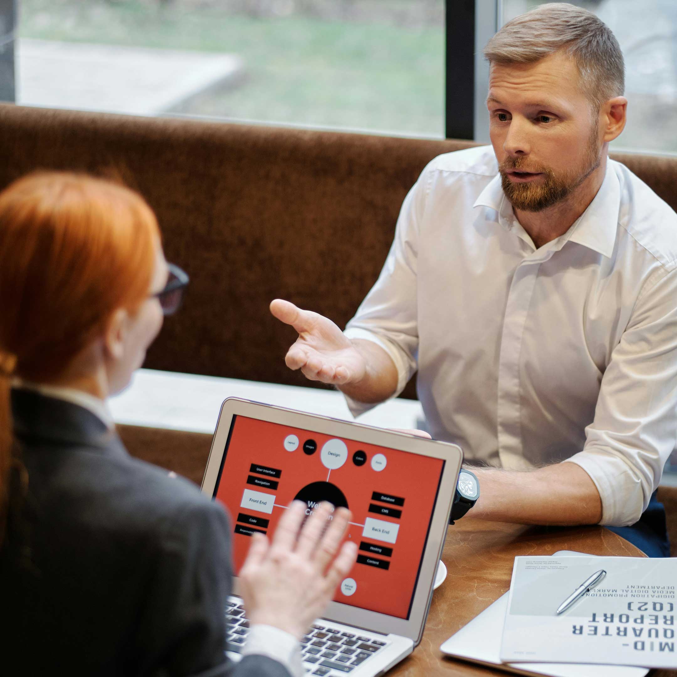 Image of a man and a woman having a conversation while the woman is referencing infographics displayed on a laptop screen
