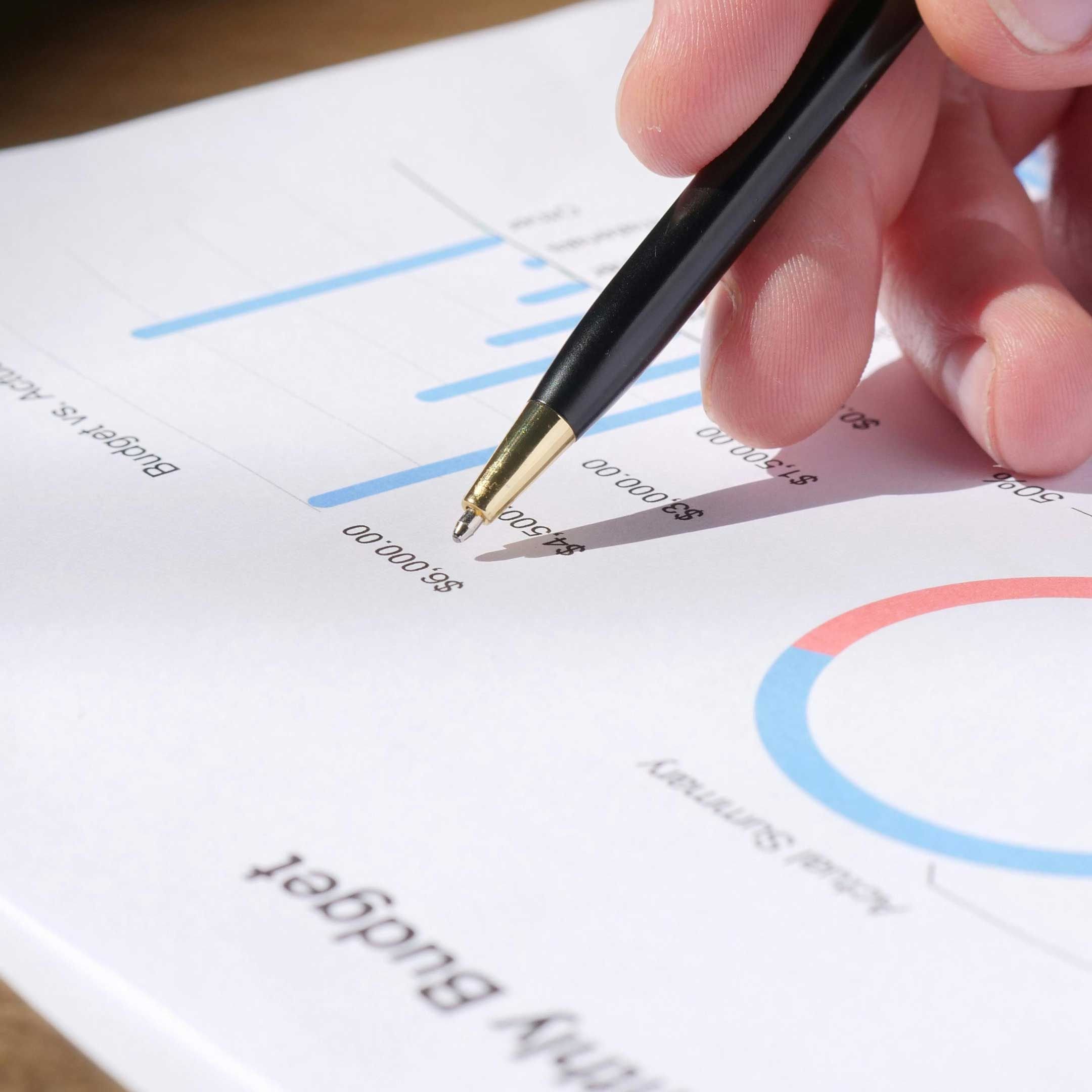 Image of a person's hand holding a pen pointing at financial information printed on a piece of paper